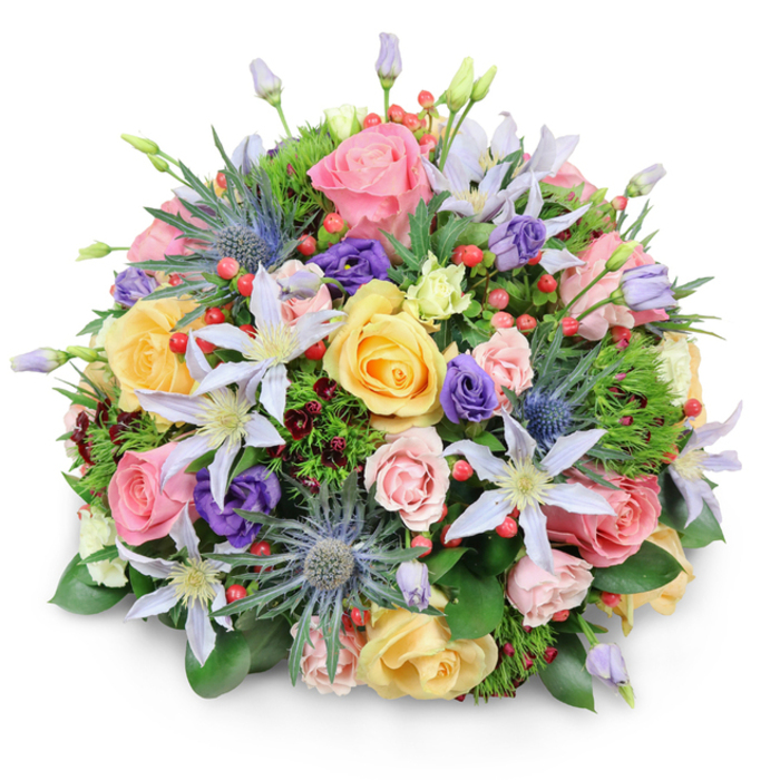 A beautifully composed domed bouquet sits centred against a crisp white background, its full, rounded silhouette casting only the softest shadow, as if floating. The flowers are densely packed, creating a tapestry of pastel and jewel tones that immediately evokes the feeling of an abundant garden in bloom, carefully curated by an experienced florist in Whitechapel. Large garden roses dominate the composition, each bloom a swirl of delicate petals in shades of pale pink, buttery yellow, and creamy peach. Some roses are wide open, revealing intricate centres, while others are partially closed, their outer petals still cupped protectively. Among these classic blooms appear several clematis flowers, their star-shaped petals in white and pale lavender stretching outward with a graceful, slightly wild elegance; their pale yellow or ivory centres add gentle points of light throughout the bouquet. Spiky blue eryngium - also known as sea holly - rise between the softer shapes, their metallic blue-grey thistle heads providing structure and a modern, textural counterpoint. Nestled around them are deeper purple lisianthus, some tight in bud and others beginning to unfurl, offering a velvety richness of colour. Scattered throughout are clusters of small, round hypericum berries in a vivid red, catching the eye like tiny lanterns and introducing a cheerful contrast. The whole design is supported by layers of greenery: broad, glossy leaves similar to camellia or laurel, delicate feathery sprigs, and occasional hints of dark burgundy foliage peeking through. The lighting is even and natural, gently illuminating the subtle colour transitions and the fine veining on the petals. The impression is of a luxurious hand-tied bouquet, ideal as a centrepiece for a dinner near Whitechapel Gallery, a romantic surprise delivered to a flat off Commercial Street, or a thoughtful gesture to brighten a colleague's day in a nearby office.